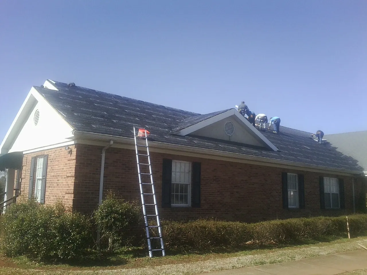 Crew tearing shingles off a brick ranch roof with a ladder set — Metal Roof Repair work by our crew in Chino