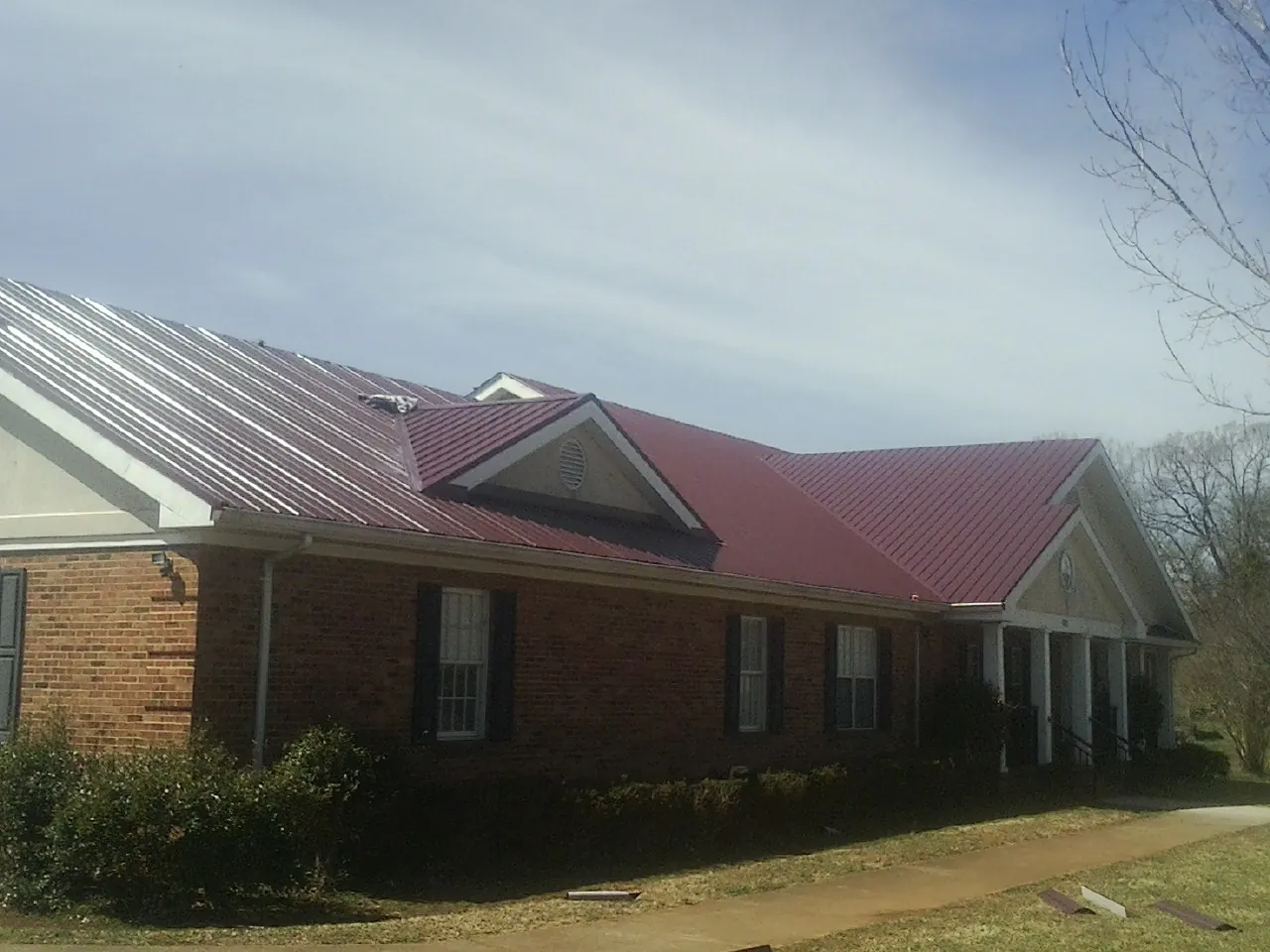 Red metal roof with gabled entries on a long brick building, from a Hail Damage Roof Repair job in Chino