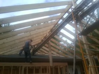 Rafters going up over a new addition with a worker on the wall in Chino