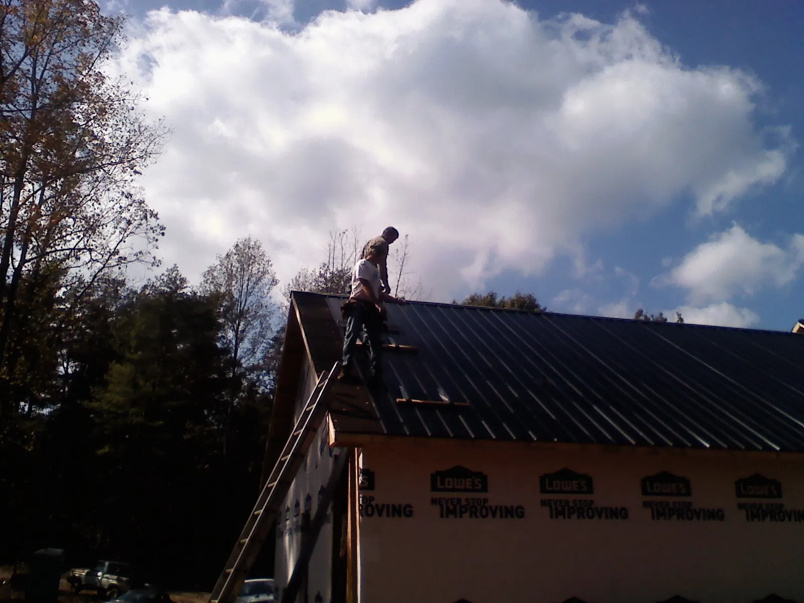 Roofer fastening dark metal panels high against a cloudy sky, from a Roof Inspection job in Chino
