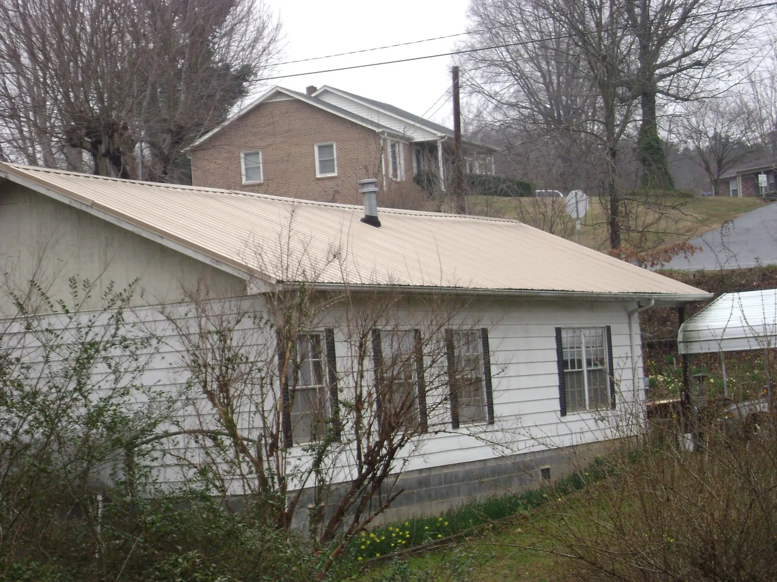 Tan metal roof on a white sided house set into a hillside — Commercial Roofing by Roofing Brothers in Chino